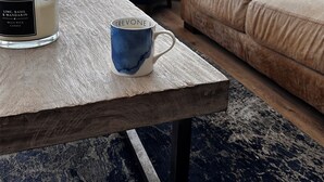 Un salon avec une grande fenêtre, une tasse bleue, une bougie et un fauteuil bleu.