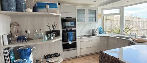 A modern kitchen with built-in appliances, a dining area with wicker chairs, and a view of the outdoors.