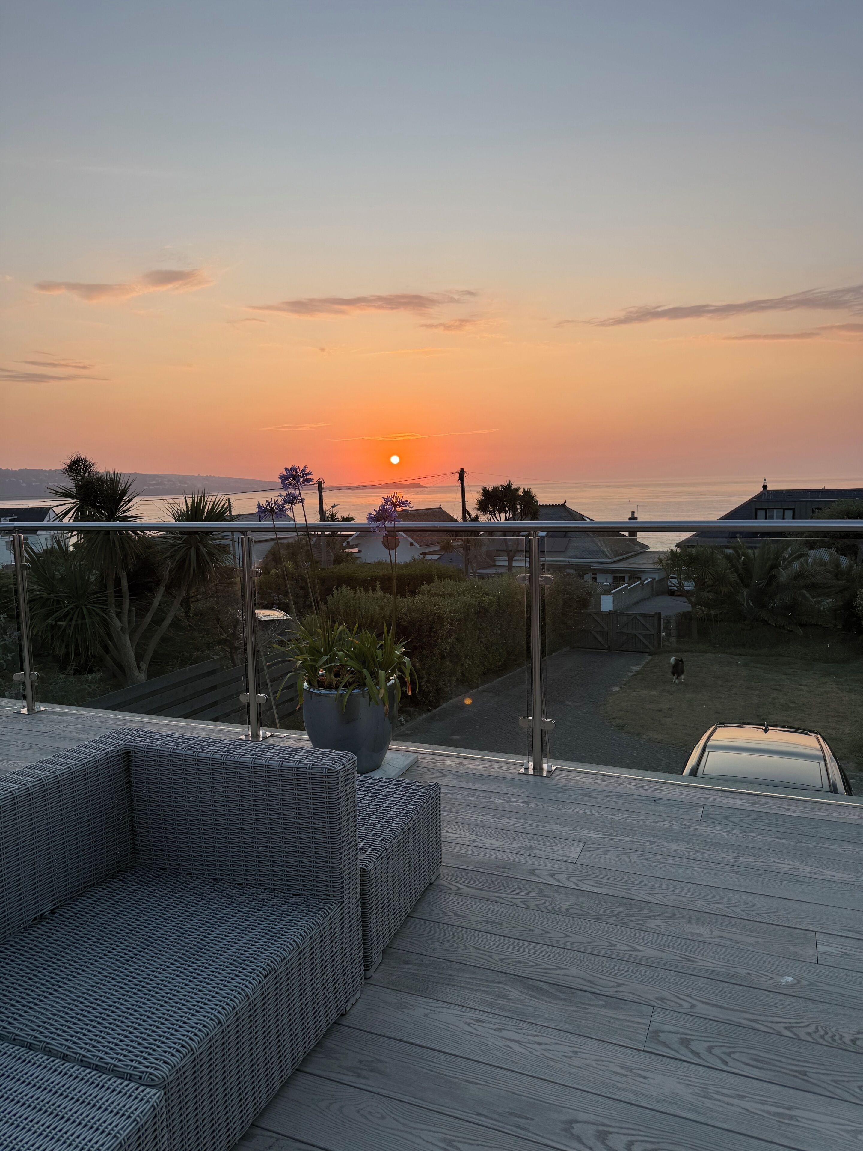 A sunset view from a balcony with a wicker sofa and a potted plant.