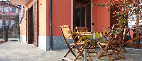 An outdoor seating area with wooden chairs and a table, a potted plant, and a building with orange walls and a door.