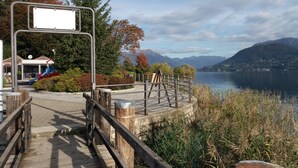 En træpromenade der fører til et søområde med en legeplads og udsigt til bjerge.