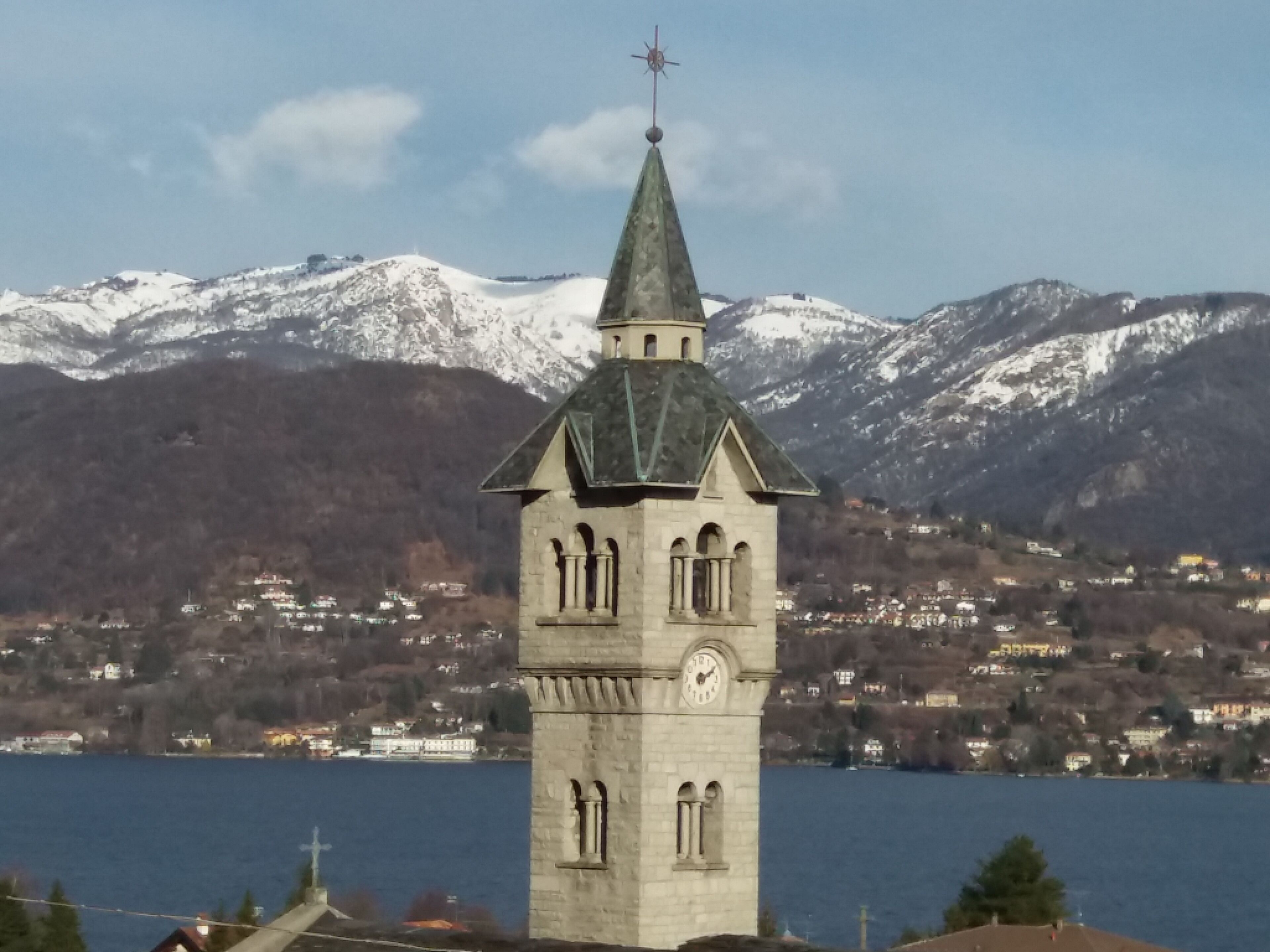 A tower with a clock, surrounded by a lake and mountains.