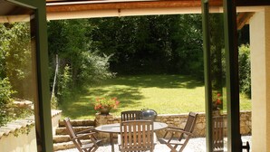 Une terrasse extérieure avec une table ronde et quatre chaises, entourée d’un mur de pierre et d’une pelouse verdoyante.