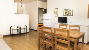 Un espacio habitable compacto con kitchenette, zona de comedor con muebles de madera y televisor.