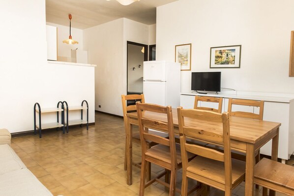 A compact living space with a kitchenette, a dining area with wooden furniture, and a television.