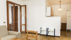 Una habitación con una mesa de comedor de madera, un sofá, una silla, una zona de cocina con mostrador y armarios, y una puerta que da a otra habitación.