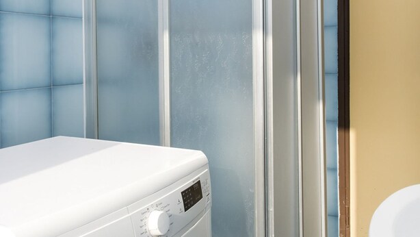 Una lavadora blanca en un baño con paredes cubiertas de azulejos azules y una pared color beige.
