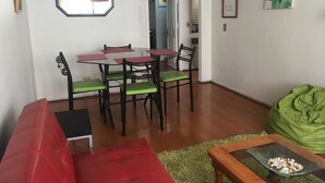 A dining area with a round table and chairs, a red sofa, a green bean bag, and a small table with snacks. - The Golf with large terrace (Las Condes)