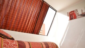 A room with a bed, a window with blinds, a wall-mounted telephone booth artwork, and a visible door. - The Golf with large terrace (Las Condes)