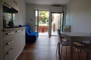 A compact kitchen with a dining area, a blue sofa, and a view through an open door to an outdoor patio.