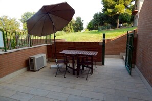 An outdoor patio with a table and chairs, a large umbrella, and a brick wall. - S127 - Sirolo, brand new studio with terrace (Sirolo)
