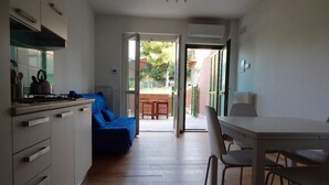 A compact kitchen with a dining area, a blue sofa, and a view through an open door to an outdoor patio. - S127 - Sirolo, brand new studio with terrace (Sirolo)