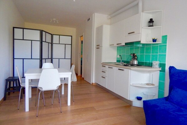 A compact kitchen with white cabinets, a green backsplash, and a dining area with a white table and chairs.