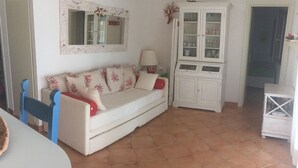 Un saló amb un sofà blanc, una cadira blava, un moble amb portes de vidre i un mirall a la paret.