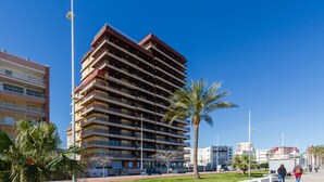 A multi-story building with balconies, a palm tree, and a clear blue sky. - LUXURY APARTMENT APARTMENT 11 with direct views of the sea, sunrises live. (GANDIA PLAYA)