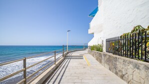 A coastal walkway with a railing, a stone wall, and a blue awning. - Aguila Beach Ocean View By CanariasGetaway (Maspalomas)