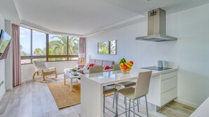 A modern, open-plan living and dining area with a kitchen, large windows, and a view of palm trees. - Aguila Beach Ocean View By CanariasGetaway (Maspalomas)