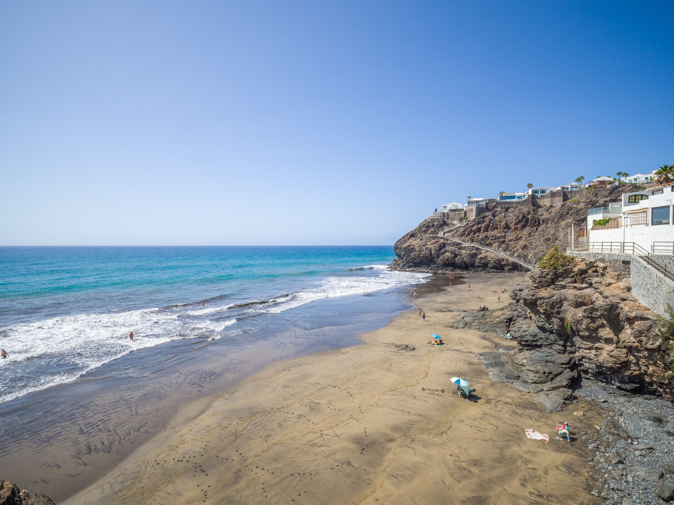 A coastal beach with rocky cliffs and a clear blue sky.