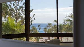 A room with a large window overlooking a beach and palm trees. - Aguila Beach Ocean View By CanariasGetaway (Maspalomas)