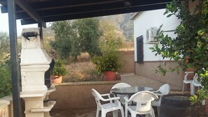 An outdoor patio with a pergola, white plastic chairs, a round table, and potted plants. - Holiday home Villa Carmeli (Ardales)