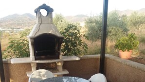 An outdoor patio with a stone table and white plastic chairs, a stone barbecue grill, and a brick wall. - Holiday home Villa Carmeli (Ardales)