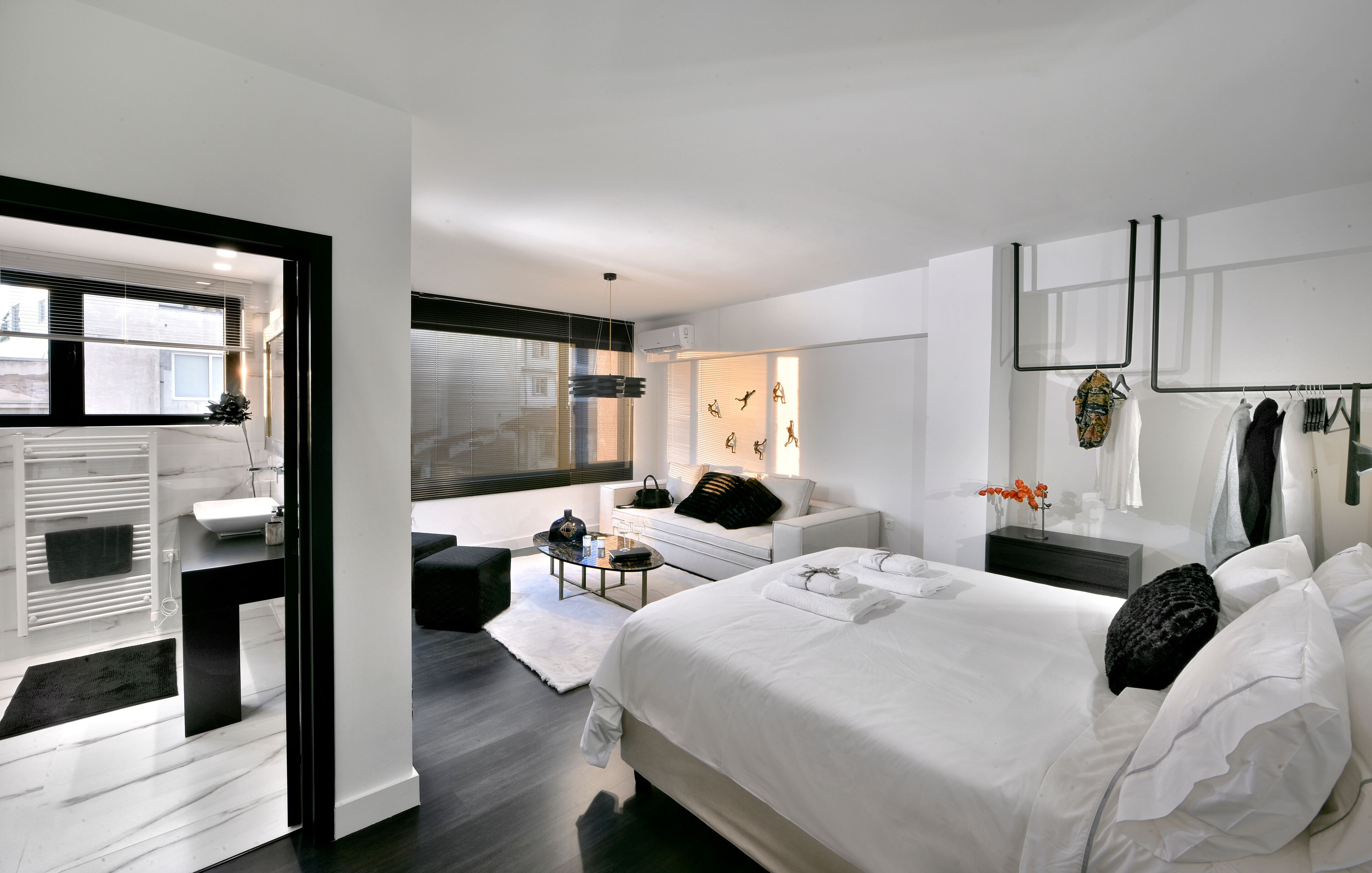 Una camera da letto moderna con un letto grande, una zona salotto con divano e tavolino, e vista sulla città attraverso ampie finestre.