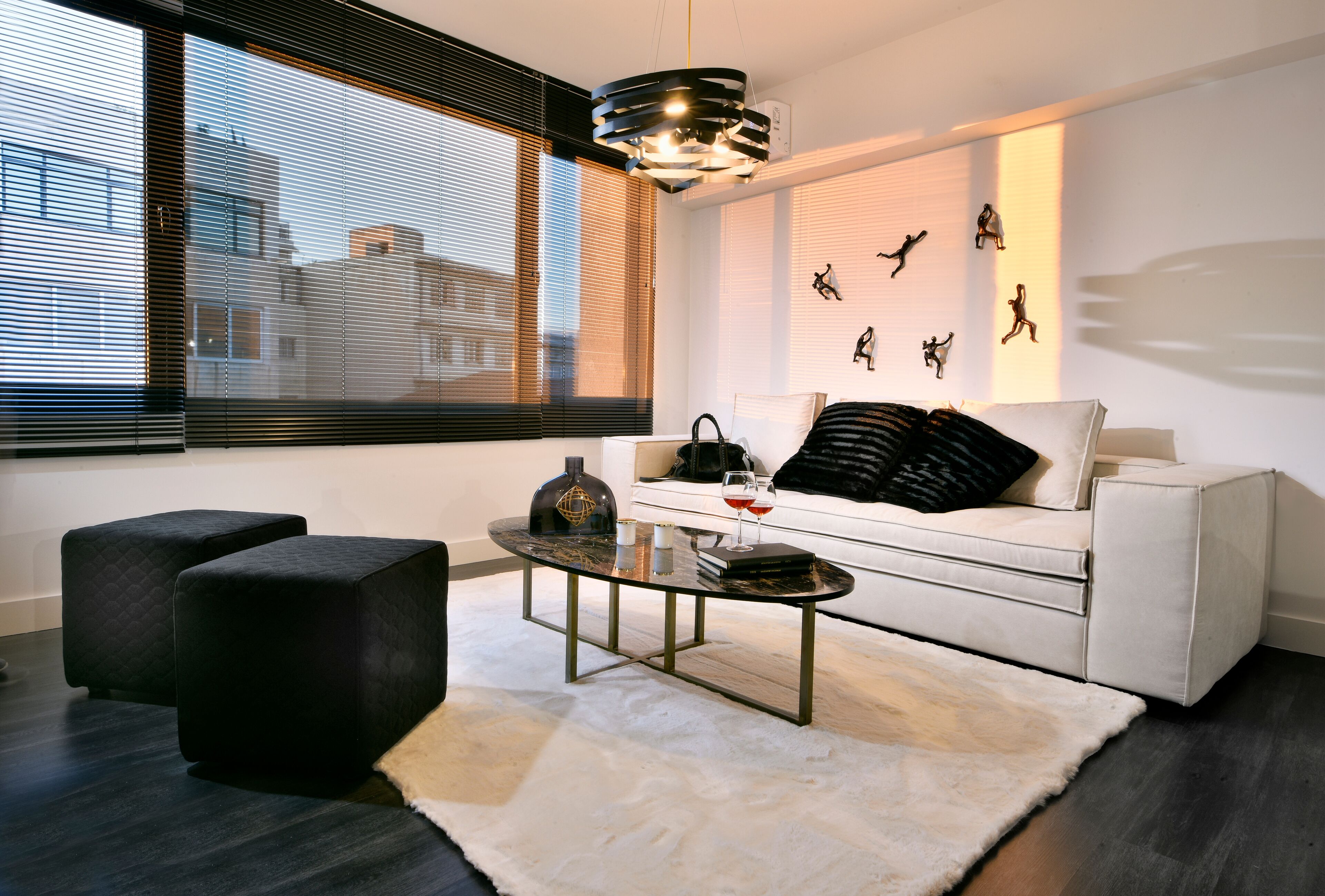 A modern living room with a white sofa, black ottomans, a glass coffee table, and a fur rug.
