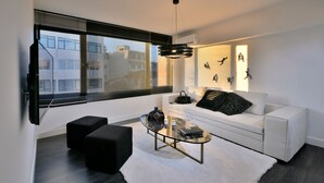 Una sala de estar moderna con un sofá blanco, otomanas negras, una mesa de centro de vidrio y un televisor montado en la pared.