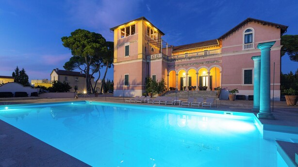 A large swimming pool with lounge chairs, a building with a tower, and a well-lit outdoor area.