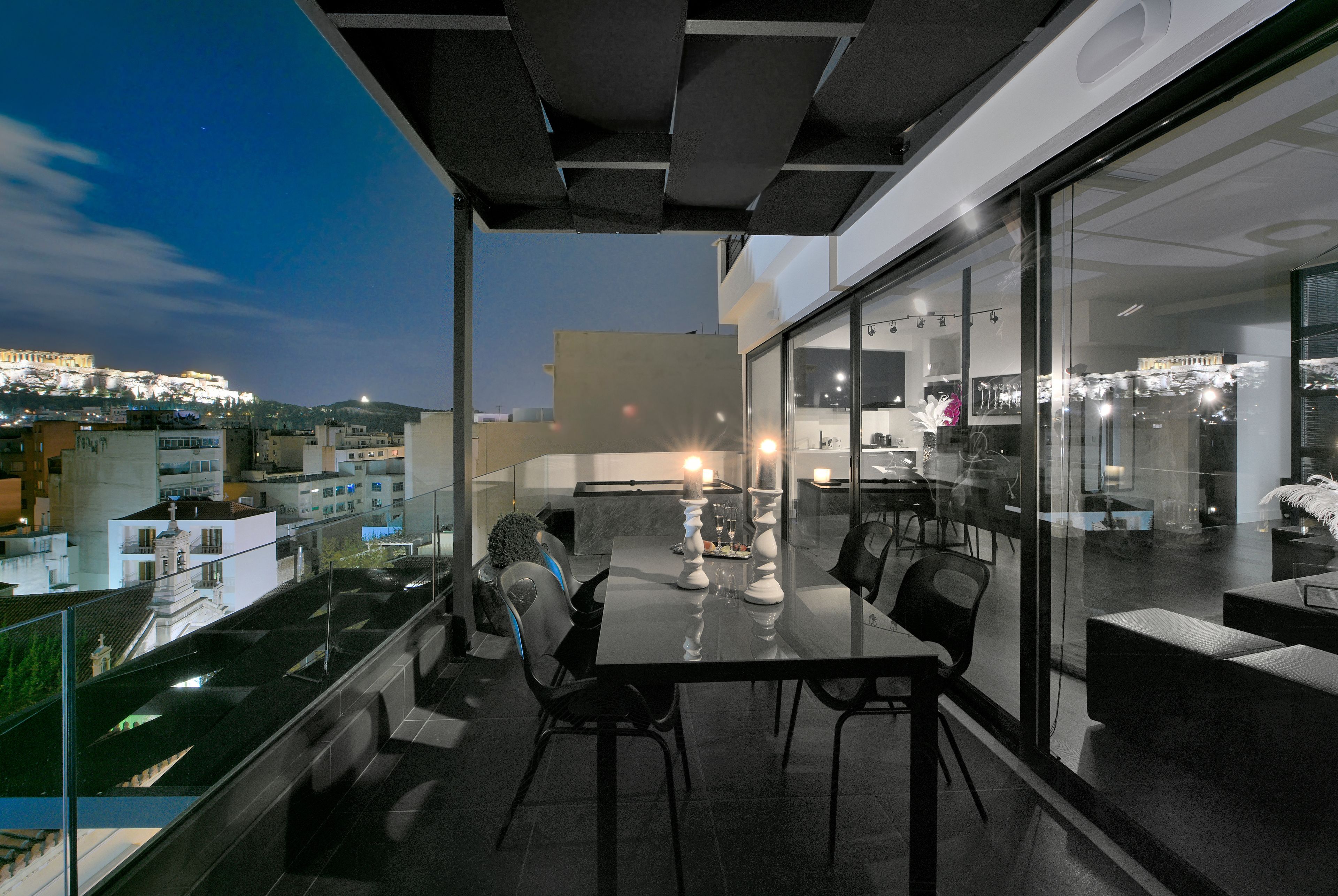 Een balkon met een glazen tafel en stoelen, met uitzicht op een stadsbeeld in de schemering.