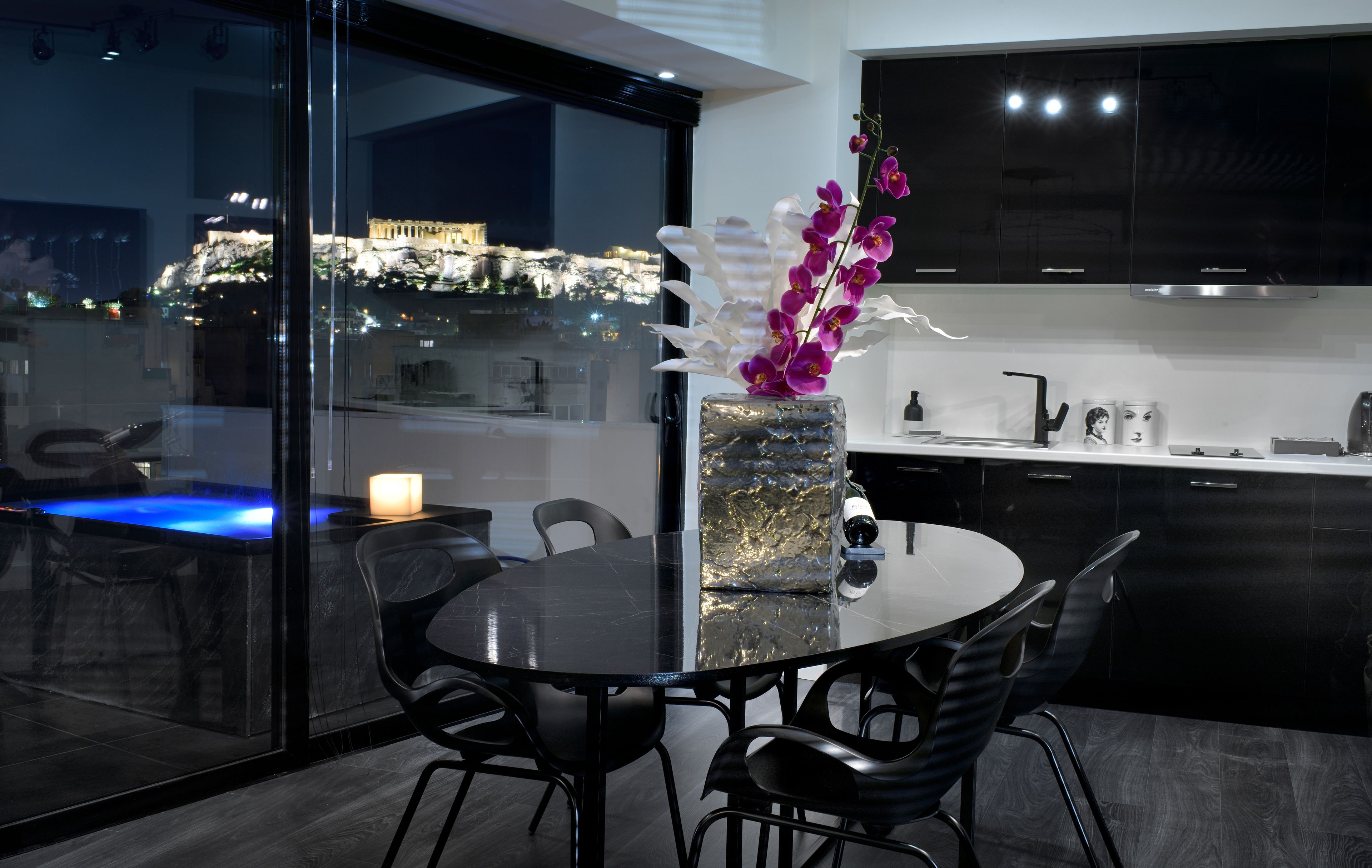 A modern kitchen with dark cabinetry, a round dining table, and a vase with purple orchids.