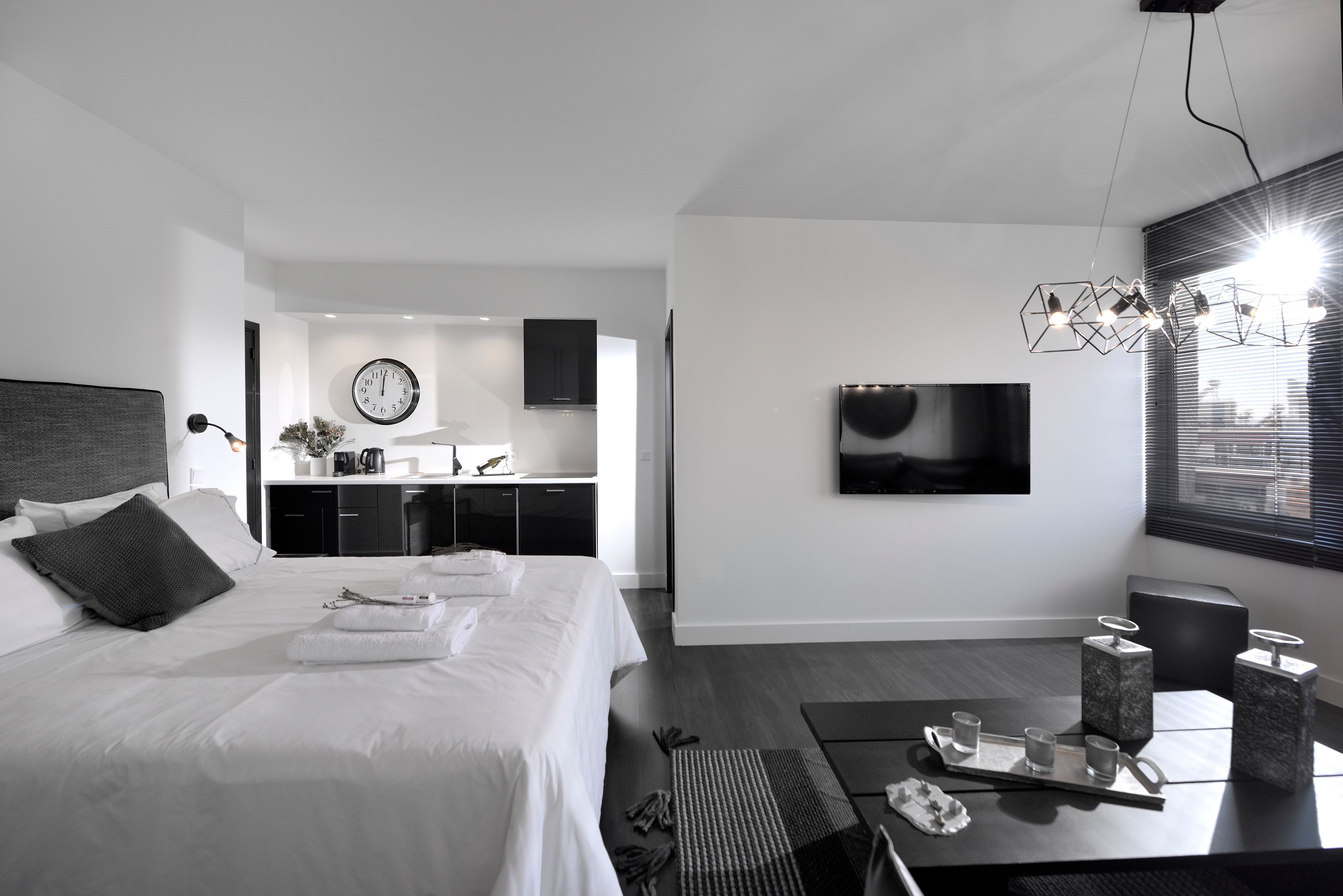 Ein modernes Hotelzimmer mit einem großen Bett, einem Essbereich mit Tisch und Stühlen, einer Küchenzeile und einem an der Wand montierten Fernseher.