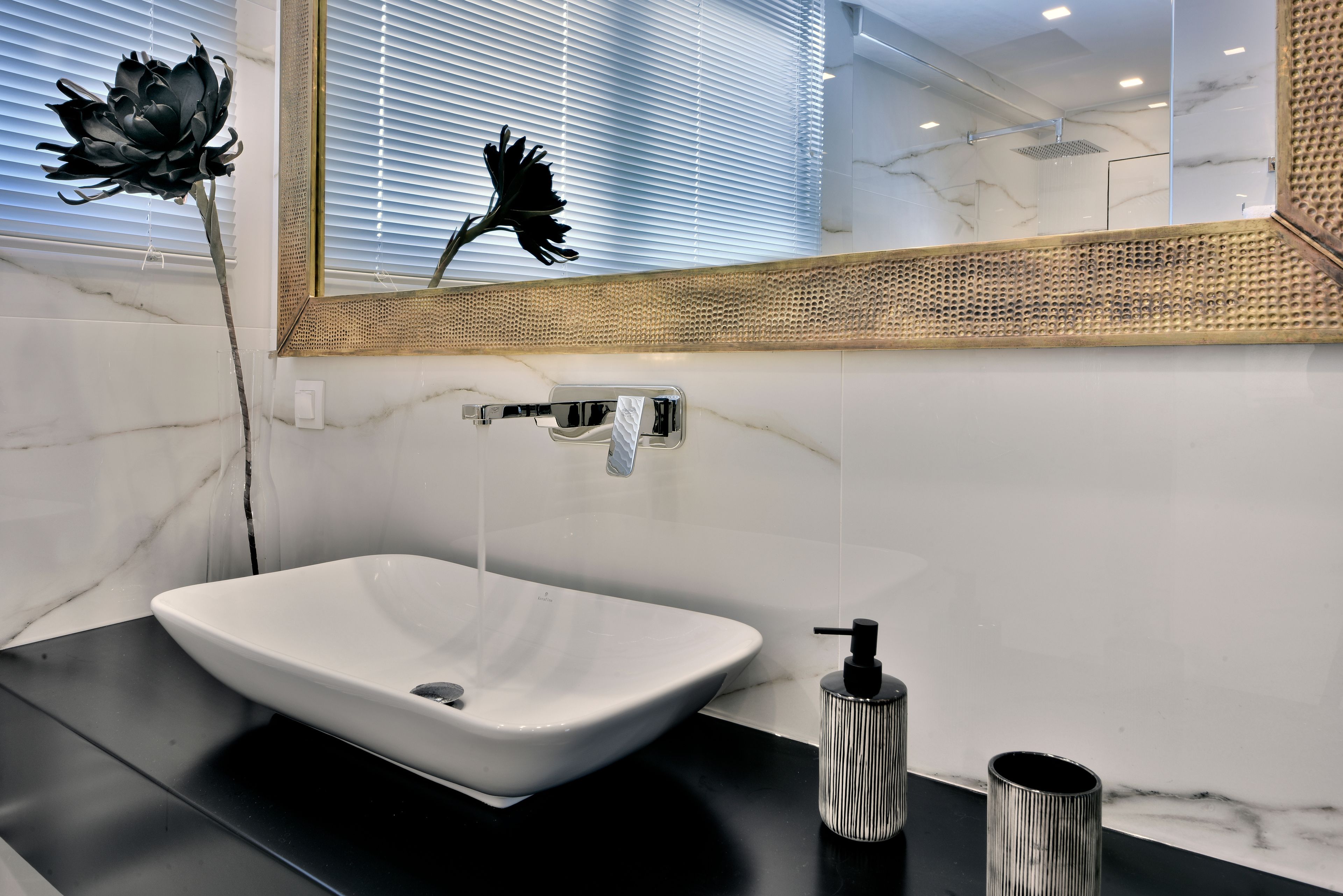 A modern bathroom with a white marble sink, a black countertop, and a large mirror with a wooden frame.