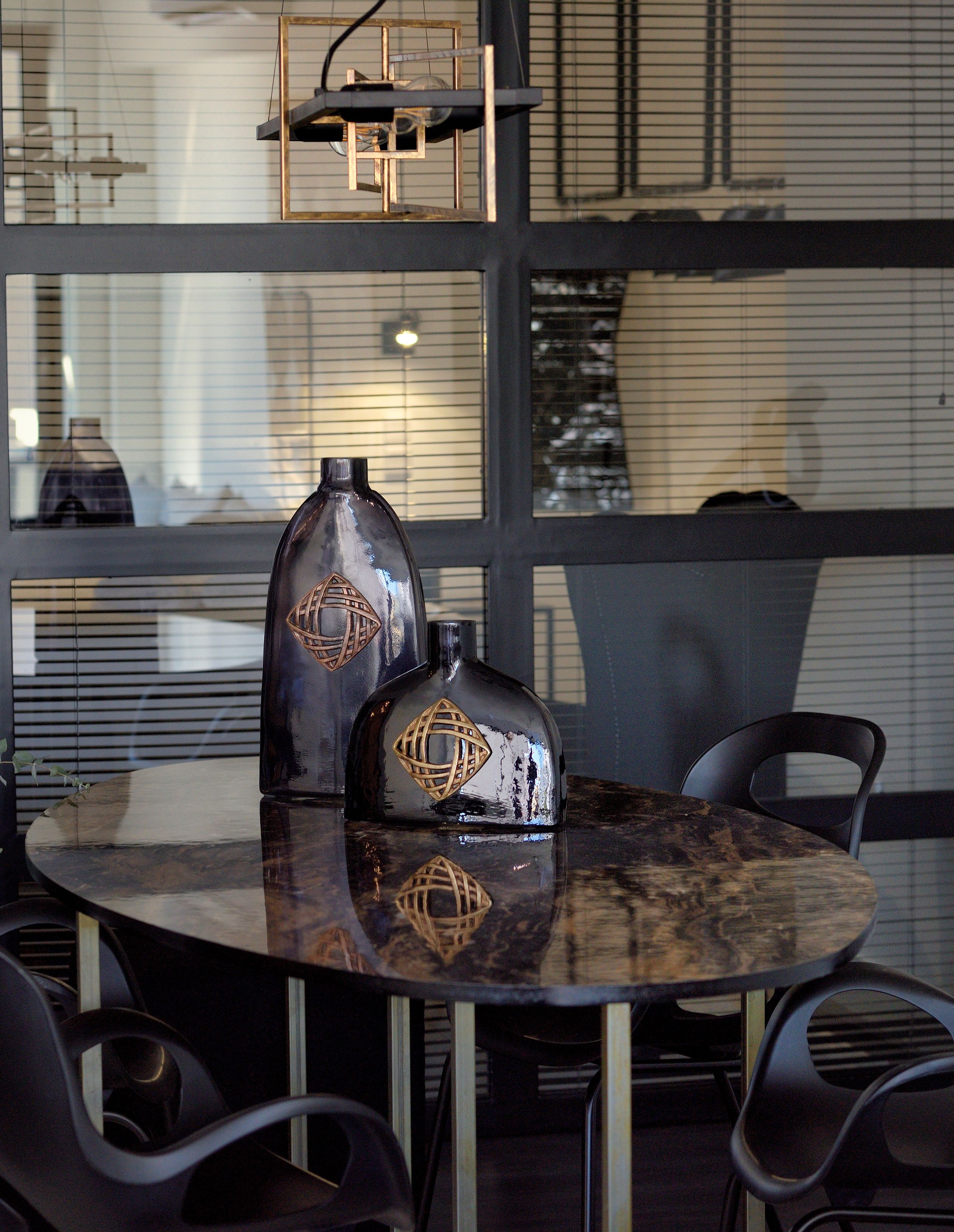 A round table with two decorative vases and a modern chair. The room features a large window with blinds and a metal shelf above the table.