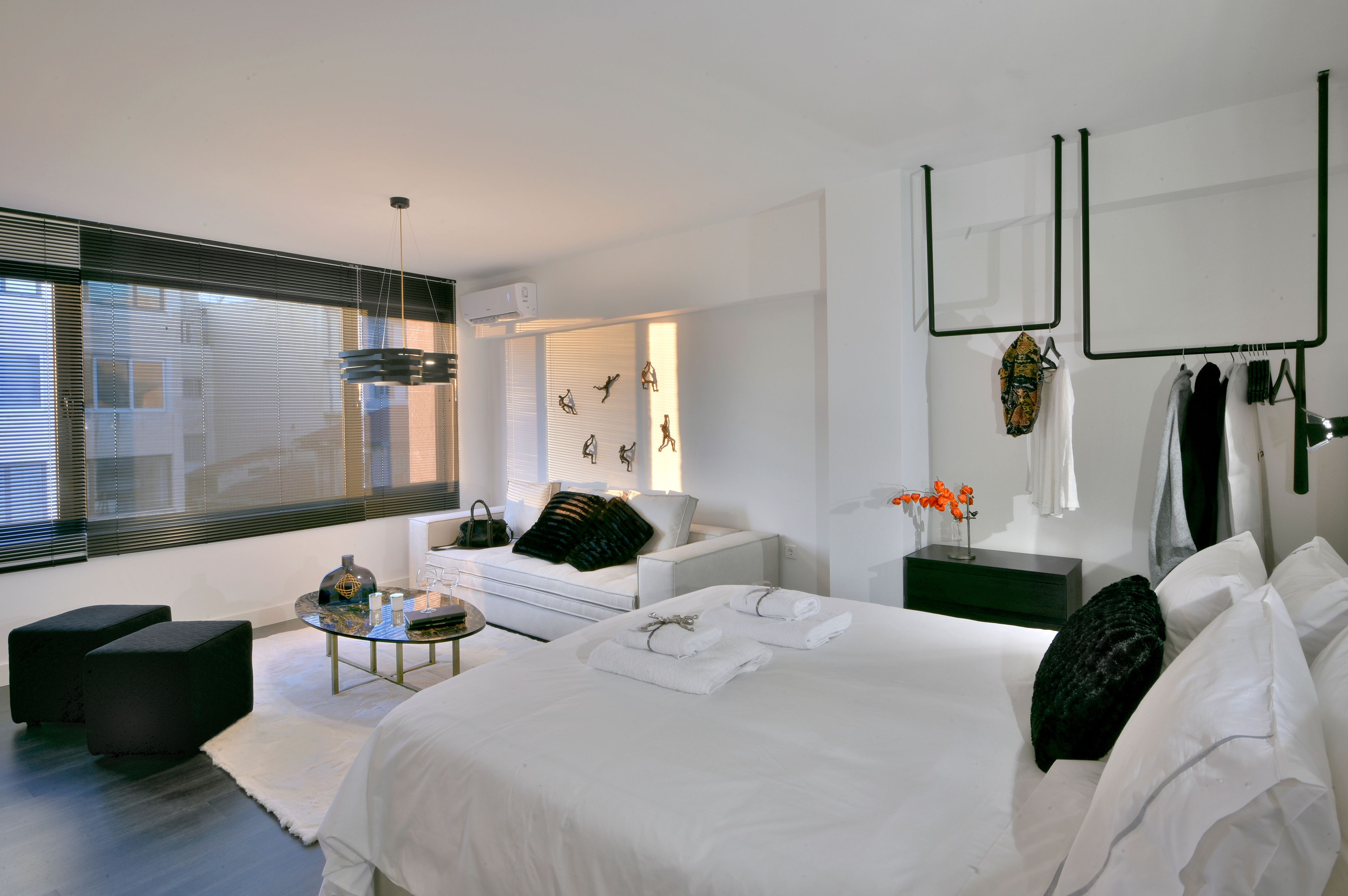 Une chambre moderne avec un grand lit, un coin salon comprenant un canapé et une table basse, ainsi qu’un étendoir fixé au mur.