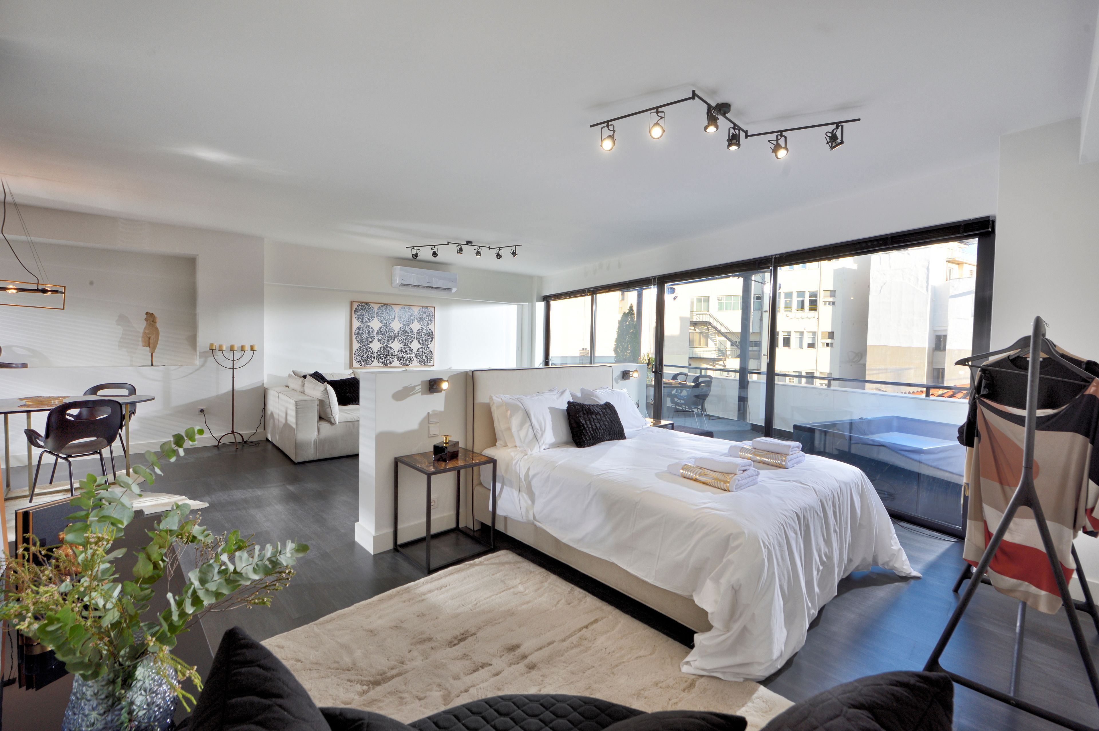 Una habitación de hotel moderna con una cama grande, un balcón, zona de comedor y vistas a la ciudad.