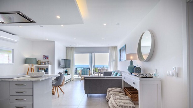 A modern living room with a sofa, a dining area, and a balcony with a view. - 1K Waterside - Praia da Luz (Luz)