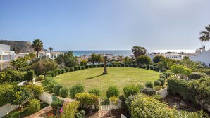 A landscaped garden with a circular lawn, palm trees, and a view of the sea. - 1K Waterside - Praia da Luz (Luz)