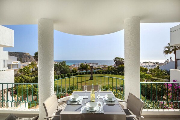 A dining table set for two with a view of the sea and a green lawn in the background.