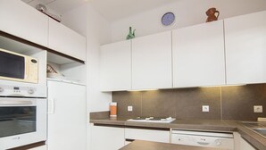 A modern kitchen with white cabinets, a built-in oven, microwave, and dishwasher. There is a magazine on the counter and a small decorative item on the wall.