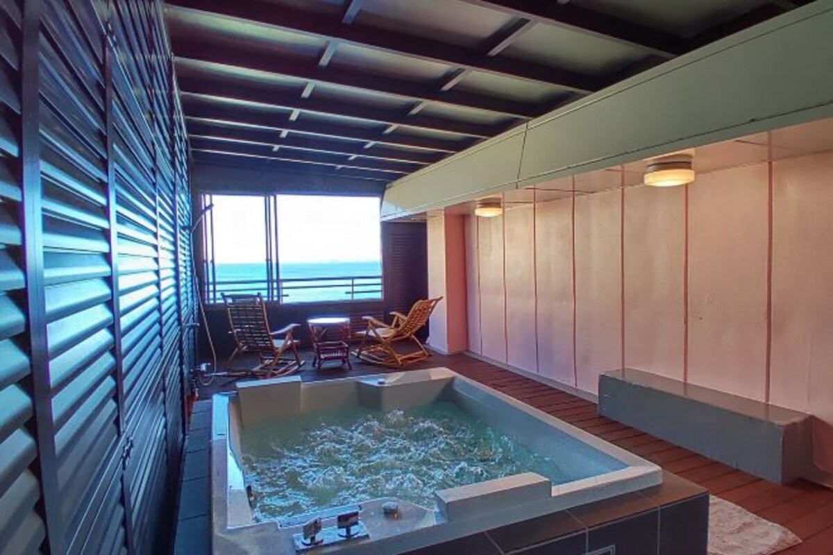 A spa area with a hot tub, wooden flooring, and a view of the ocean.