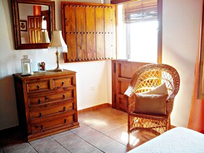 Una habitación con cómoda de madera, silla de mimbre y ventana con persianas.