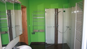 Ein Badezimmer mit grüner Wand, Waschbecken in Weiß, einer Duschkabine aus Glas und einem Handtuchhalter.
