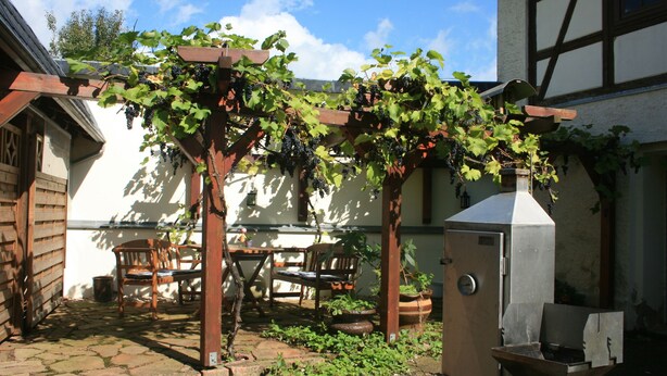 Eine rustikale Terrasse im Freien mit einer Holz-Pergola, einem Steintisch und Stühlen.