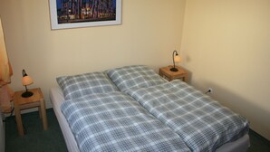 Ein Zimmer mit einem Bett, zwei Nachttischen und einem gerahmten Bild an der Wand.