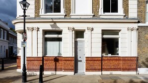 A two-story building with a classic architectural style, featuring a prominent entrance with a white door and a large window above it. - Raise the Bar, by Veeve (London)