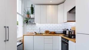 A modern kitchen with white cabinets, a wooden countertop, and a built-in oven. - Raise the Bar, by Veeve (London)