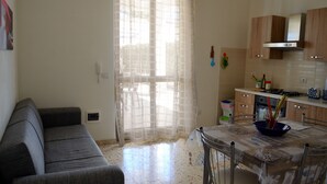 A compact living space with a sofa, a dining table with a bowl, and a kitchen area with wooden cabinets and a stove. - Brand new villa with private pool and terrace Alcamo marina (Alcamo)