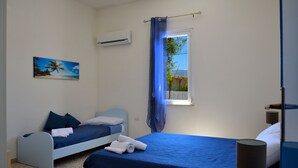 A bedroom with two beds, a window with blue curtains, a wall-mounted air conditioner, and a beach-themed painting. - Brand new villa with private pool and terrace Alcamo marina (Alcamo)