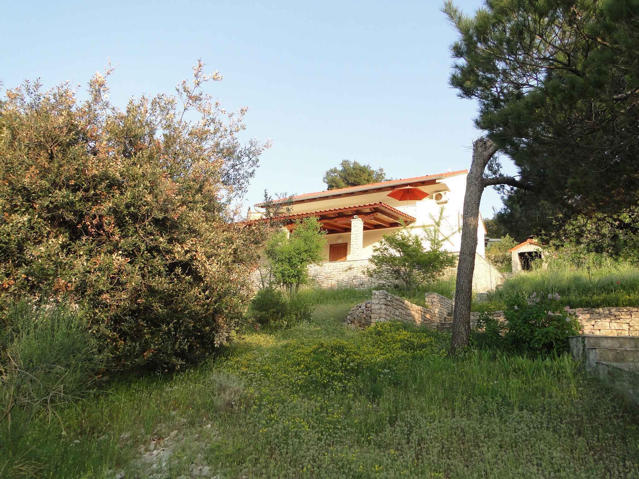 A rustic stone house with a red-tiled roof, surrounded by lush greenery and a small garden.